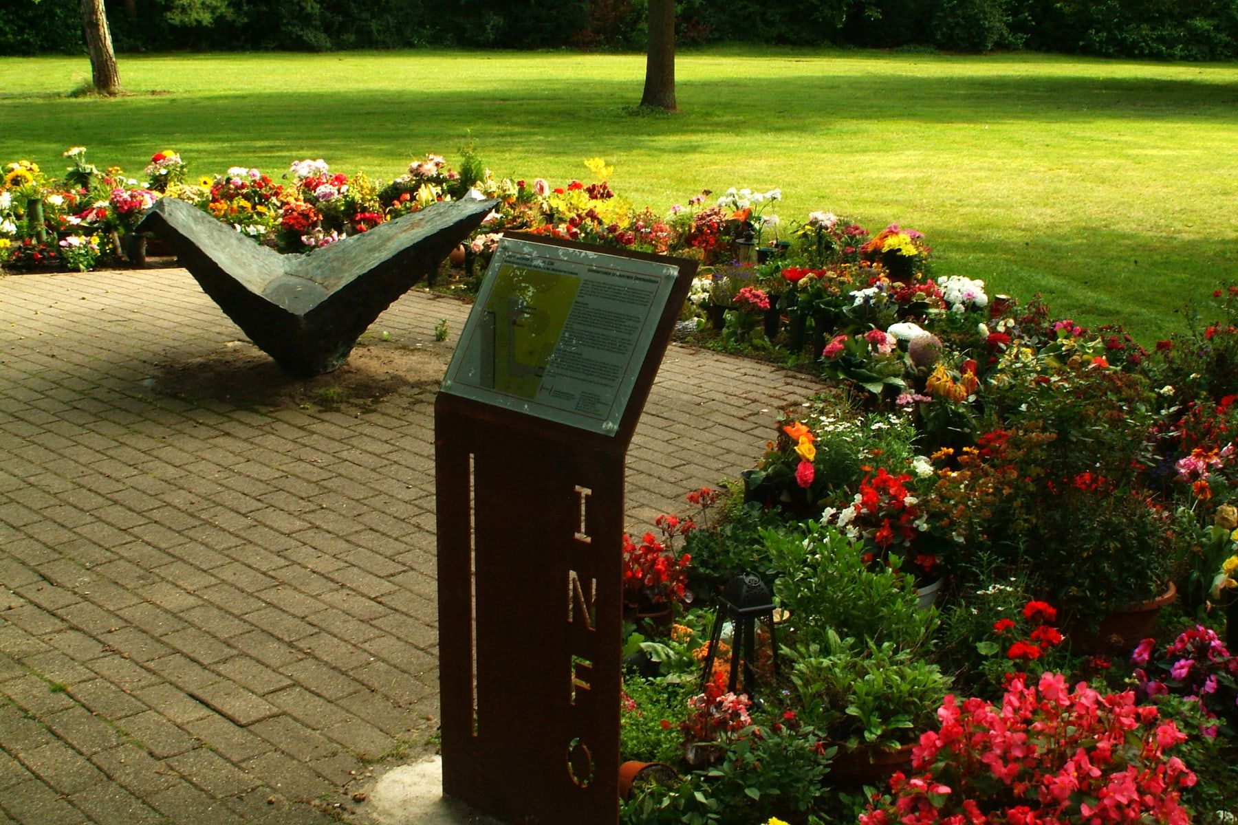 Blumenreiches anonymes Gräberfeld mit Informationstafel und schalenförmiger Skulptur auf Stadtfriedhof Lahe